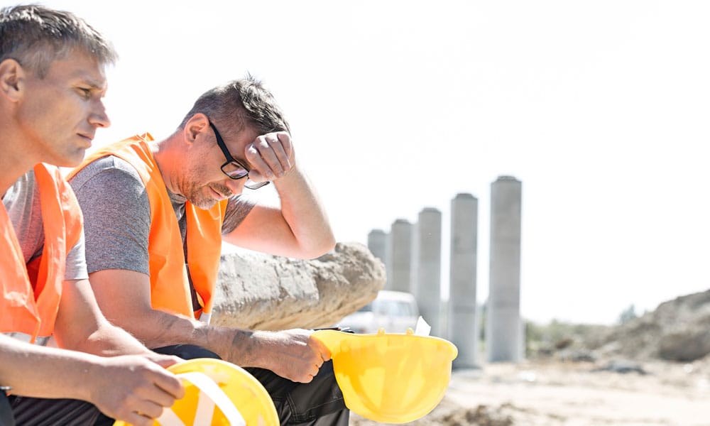 Two construction workers sitting outside being busy.